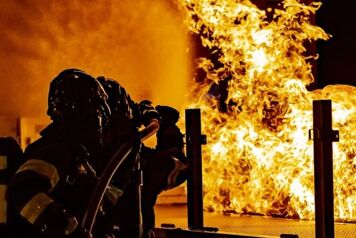 Deux sapeurs pompiers éteingnent un feu avec un tuyau la nuit