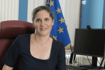 Prefet Claire Raulin assise sur son bureau avec le drapeau de l'union européenne et Français en arrière plan